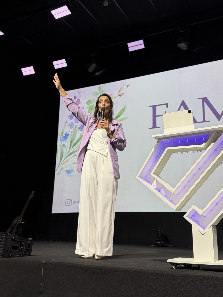 Adriana Ricci de corpo inteiro no palco, diante do telão do pilar Família.