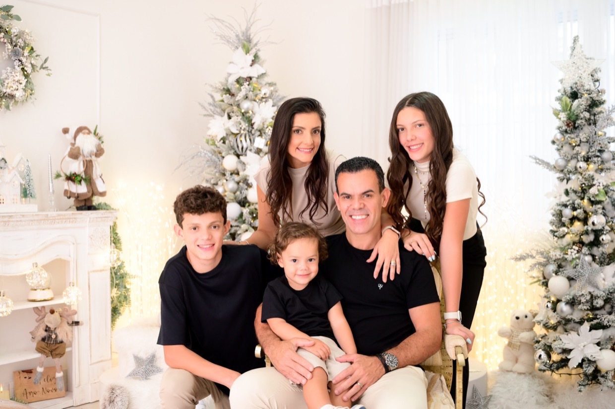 Uma família de cinco pessoas reunida e sorrindo em um estúdio de fotografia decorado.