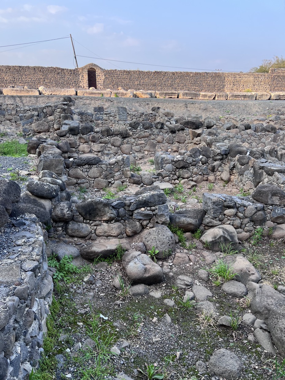Ruínas de pedra de um sítio arqueológico em Israel, com um muro antigo ao fundo.